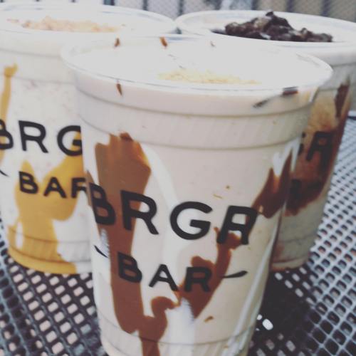 Three milkshakes in clear cups with the "BRGR BAR" logo, featuring swirls of chocolate and caramel sauces.