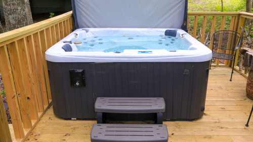 A hot tub on a wooden deck, surrounded by a railing and steps, with water visible inside.