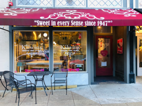 Exterior of Kilwins shop with a red awning, showcasing a welcoming entrance and outdoor seating.