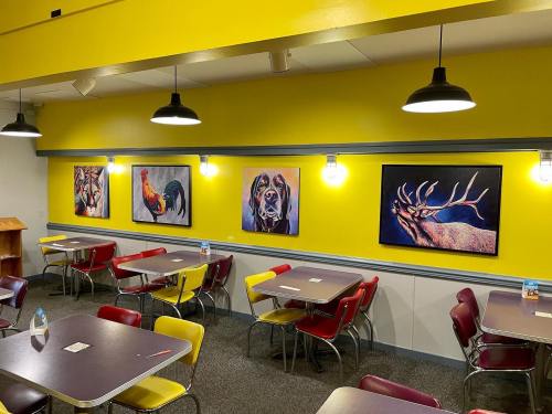 A brightly colored dining area with yellow walls, featuring animal artwork and tables with red and yellow chairs.
