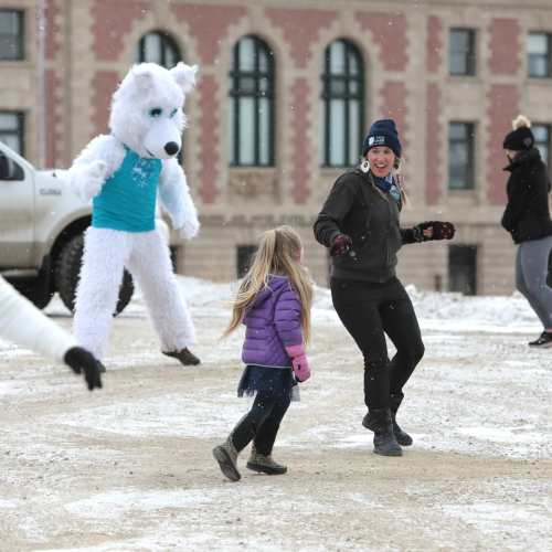 A woman and a girl play in the snow while a person in a polar bear costume dances nearby.