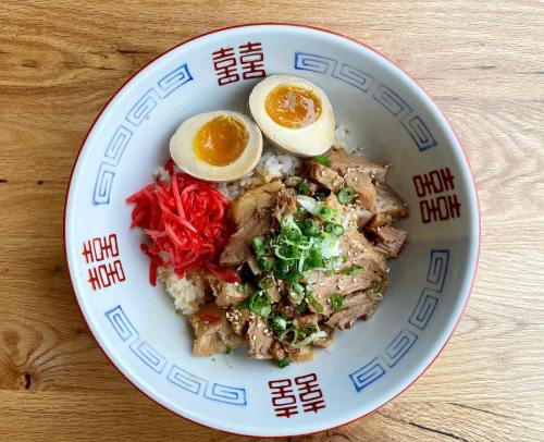 A bowl of rice topped with tender meat, green onions, pickled ginger, and two halved soft-boiled eggs.