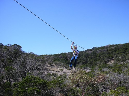 A person zip-lining through a forested area under a clear blue sky.