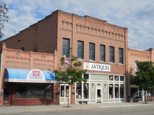 Historic brick building with "Antiques" sign, featuring large windows and a neighboring insurance agency storefront.