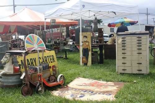 A vibrant outdoor market scene with vintage items, tents, and colorful umbrellas on a grassy area.