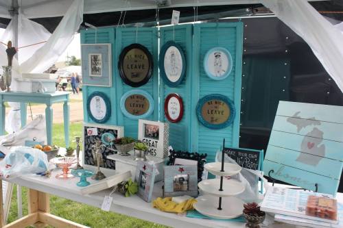 A display of decorative items and crafts on a table, featuring framed art, plates, and various home decor pieces.