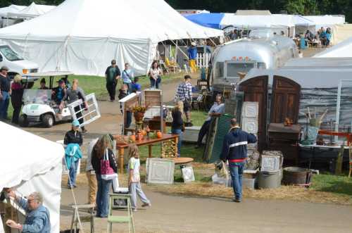 A bustling outdoor market with tents, vendors, and people browsing various handmade goods and decorations.