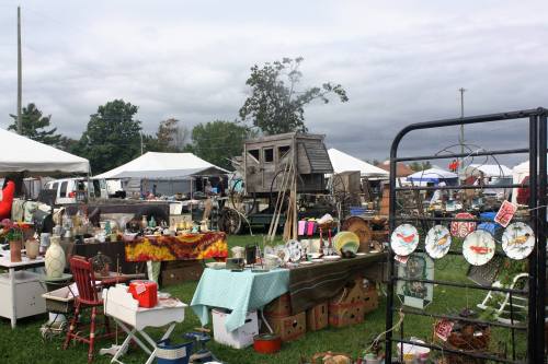 A bustling outdoor flea market with various stalls, vintage items, and tents under a cloudy sky.