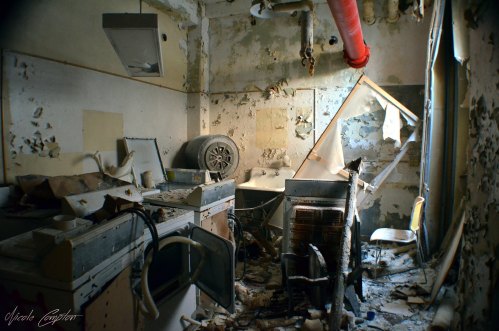 A cluttered, abandoned room with damaged walls, old furniture, and debris scattered throughout.