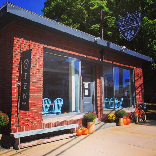 Exterior of Norway Brewing Company with large windows, blue chairs, pumpkins, and an "Open" sign.