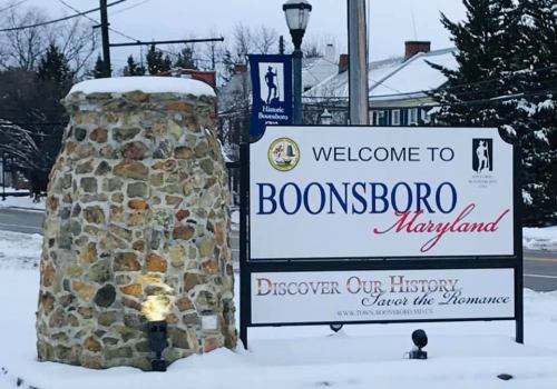 Welcome sign for Boonsboro, Maryland, surrounded by snow, featuring a stone base and historical details.
