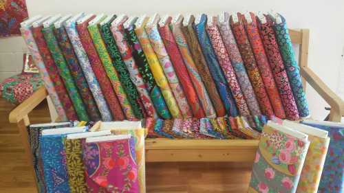 A wooden bench displaying a colorful array of patterned fabric rolls and books, showcasing vibrant designs.