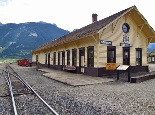 Historic train station in Silverton, surrounded by mountains, with wooden architecture and railroad tracks nearby.