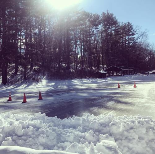 A snowy landscape with ice and traffic cones, surrounded by trees and a clear blue sky.