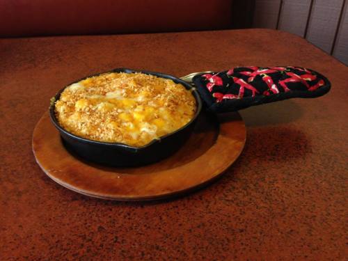 A cast iron skillet filled with baked macaroni and cheese, topped with a golden breadcrumb crust, on a wooden serving board.