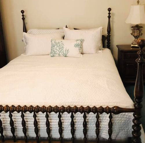 A neatly made bed with a white quilt, decorative pillows, and a bedside lamp in a cozy room.