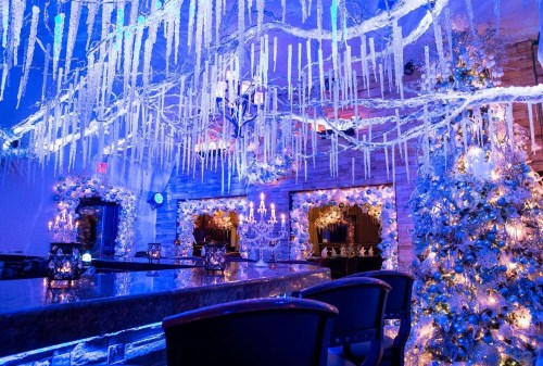 A beautifully decorated bar with icicle lights, a festive tree, and elegant floral arrangements, all in blue tones.
