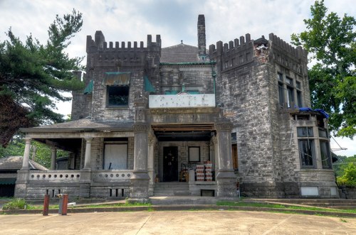 Abandoned stone mansion with gothic architecture, featuring turrets and a weathered facade, surrounded by trees.