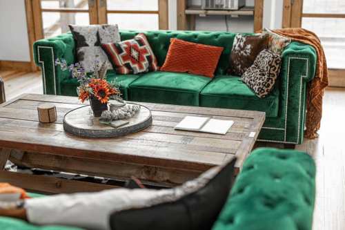 A vibrant green sofa with colorful pillows, a rustic wooden coffee table, and a floral centerpiece in a cozy living space.