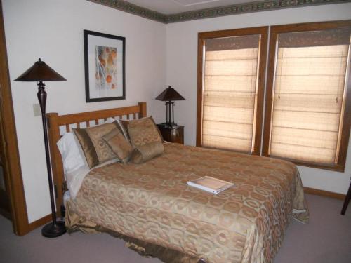 Cozy bedroom with a wooden bed, decorative bedding, two lamps, and window shades. A book rests on the bed.