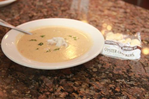 A bowl of creamy soup garnished with herbs, accompanied by a pack of oyster crackers on a granite countertop.