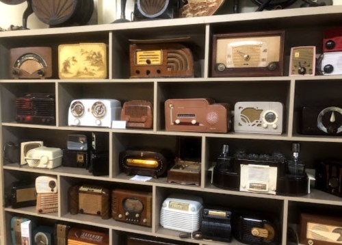 A collection of vintage radios displayed on shelves, showcasing various designs and colors from different eras.