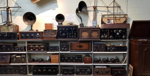 A collection of vintage radios and phonographs displayed on shelves, showcasing various designs and styles.