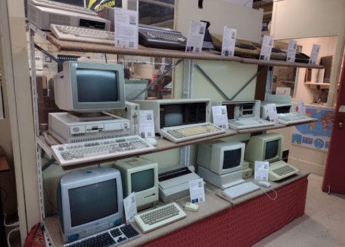 A display of vintage computers on shelves, showcasing various models and keyboards with informational tags.