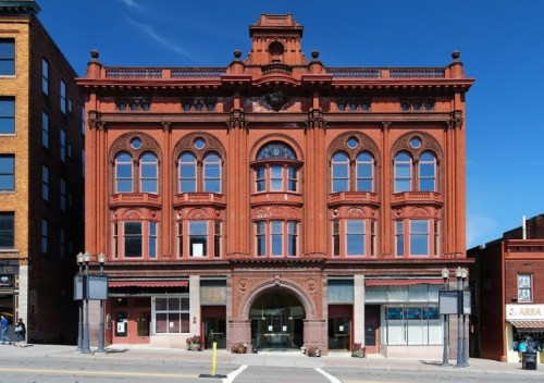 Historic red brick building with ornate architectural details and large windows against a clear blue sky.