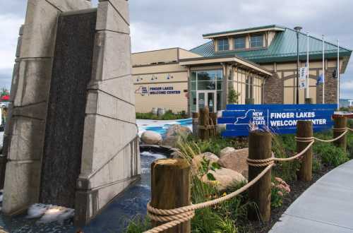 A modern welcome center with a waterfall feature, surrounded by rocks and greenery, in the Finger Lakes region of New York.