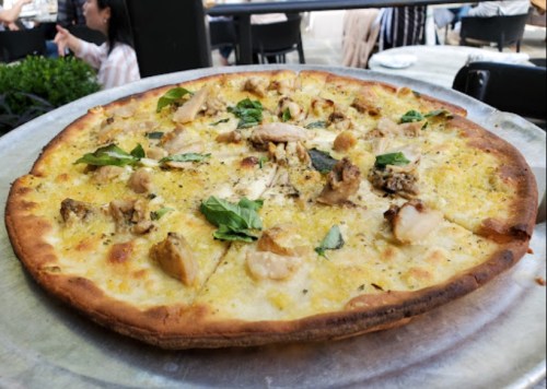 A close-up of a pizza topped with chicken, herbs, and a golden crust, served on a metal tray.
