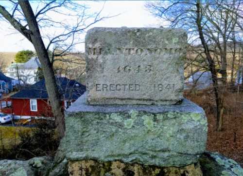 Stone monument with the inscription "HANTOMONG 1645 ERECTED 1841," surrounded by trees and buildings in the background.