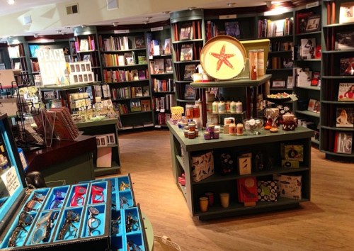 A cozy bookstore interior with shelves of books, decorative items, and a display table featuring candles and gifts.