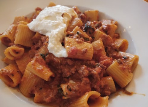 A plate of rigatoni pasta topped with a rich meat sauce and a dollop of creamy ricotta cheese.