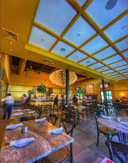 Interior of a restaurant featuring yellow ceilings, elegant lighting, and tables set for dining.