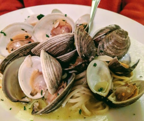 A plate of spaghetti topped with clams, garnished with herbs in a light sauce.