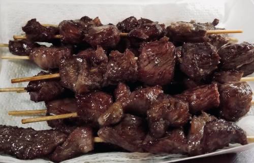 A close-up of skewered grilled meat, glistening and arranged neatly on a white paper towel.