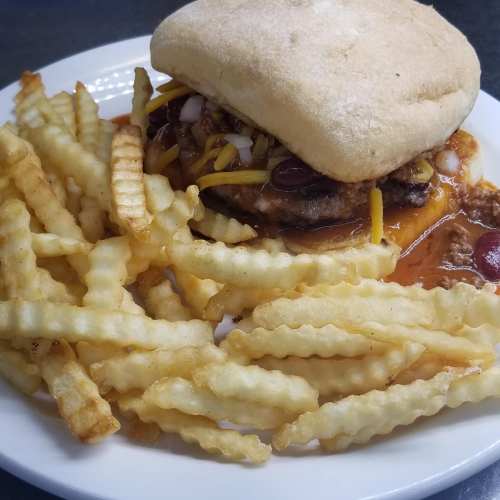 A plate with a sandwich topped with onions and mustard, served with a side of crinkle-cut fries.