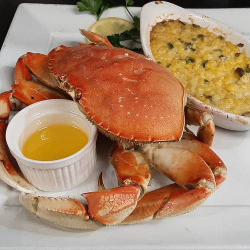 A cooked crab on a plate with a side of melted cheese and a small dish of olive oil, garnished with lemon and parsley.