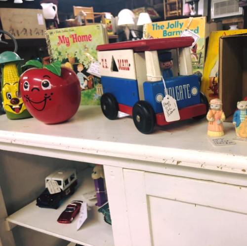 A vintage display featuring a red apple toy, a toy truck, and various nostalgic items on a white shelf.