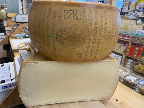 A large wheel of cheese with markings sits atop a block of cheese on a wooden counter in a shop.