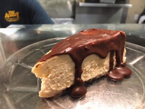 A slice of cheesecake topped with a glossy chocolate drizzle, served on a clear plate.