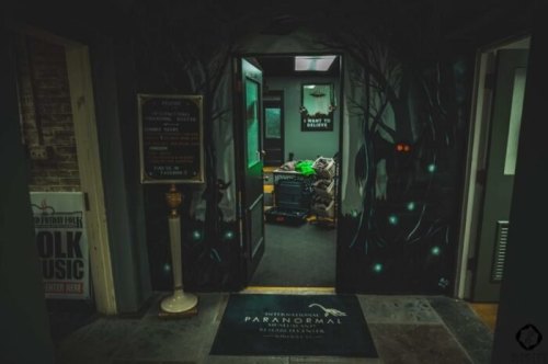 A dimly lit entrance to a paranormal investigation center, featuring eerie wall art and a welcoming sign.