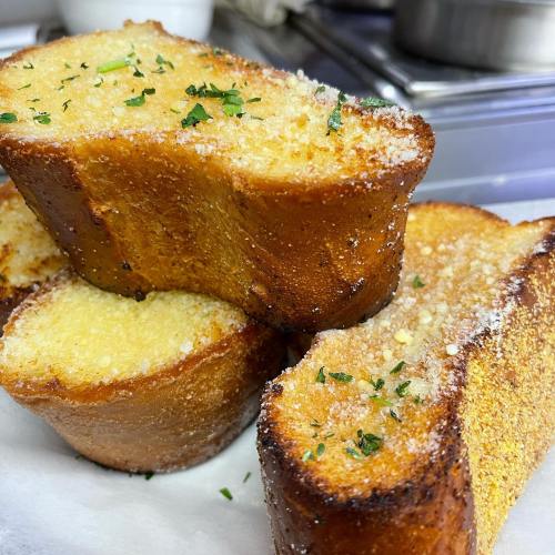 Golden-brown slices of toasted bread, topped with herbs and a sprinkle of seasoning, stacked on a white surface.