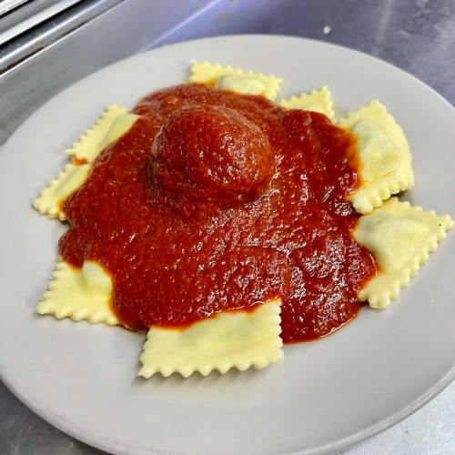 A plate of ravioli topped with marinara sauce and a meatball in the center.