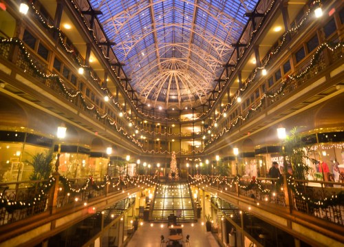 A beautifully decorated atrium with a glass ceiling, adorned with lights and festive decor for the holidays.