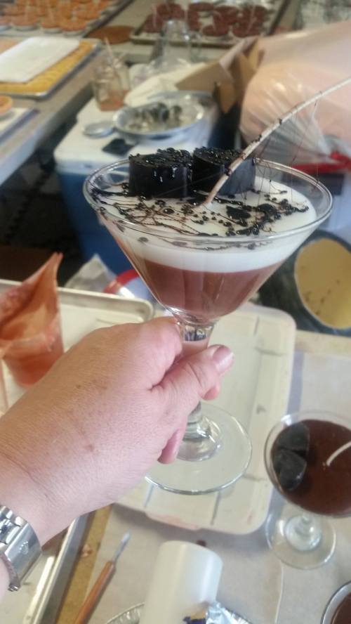 A hand holding a layered dessert in a martini glass, topped with chocolate and decorative elements.