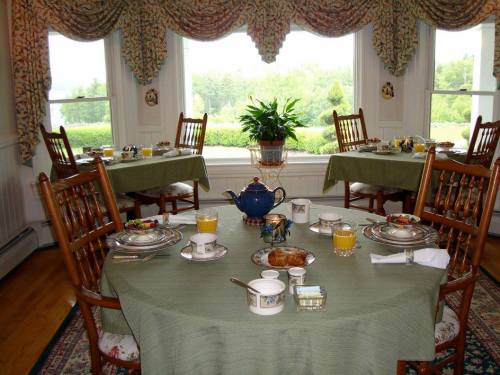 A cozy dining room set for breakfast, featuring a table with tea, fruit, and pastries, surrounded by large windows.