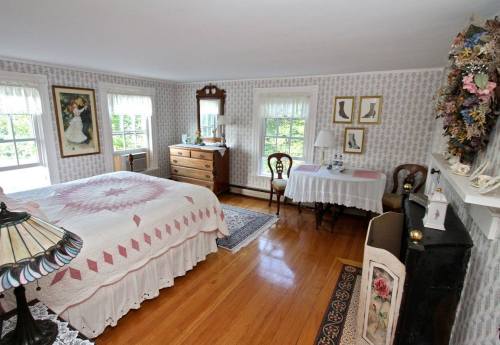 Cozy bedroom with a quilted bed, wooden dresser, and a small dining table, featuring floral wallpaper and natural light.