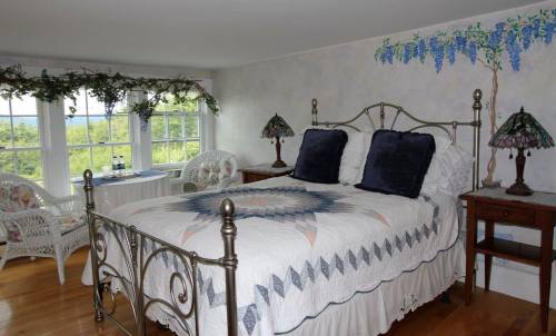 Cozy bedroom with a metal bed, decorative quilt, two lamps, and a view of greenery through large windows.